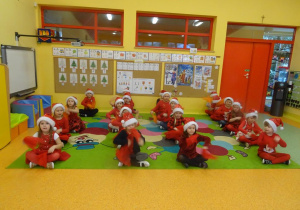 Dzieci siedzą w czterech rzędach, w ręku trzymają czerwone chusteczki.